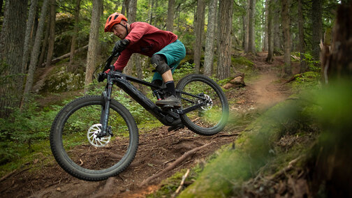 Un homme parcourt un sentier de VTT difficile à travers la forêt sur un VTT électrique, entouré d'arbres denses.