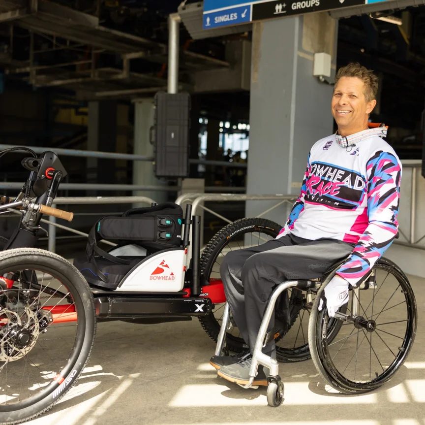 arek Rasouli sits in his wheelchair at a gondola station and smiles at the camera. 