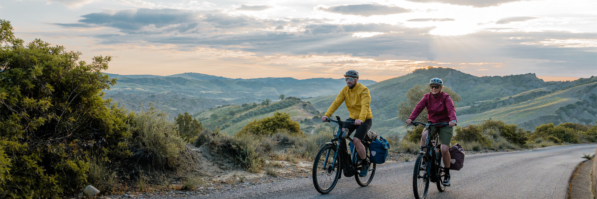 A woman and a man are riding their Trekking eBike bikes on a road, with a vast landscape in the background.