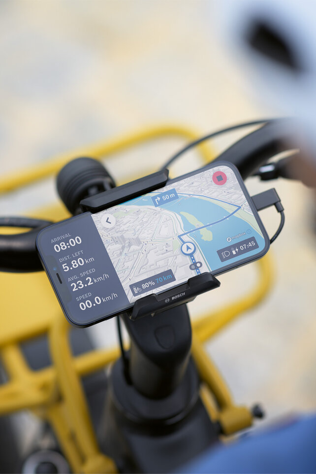 De smartphone is bevestigd aan een houder op het fietsstuur en wordt gebruikt als eBike-display voor navigatie, waarbij het route-informatie en navigatieaanwijzingen toont.