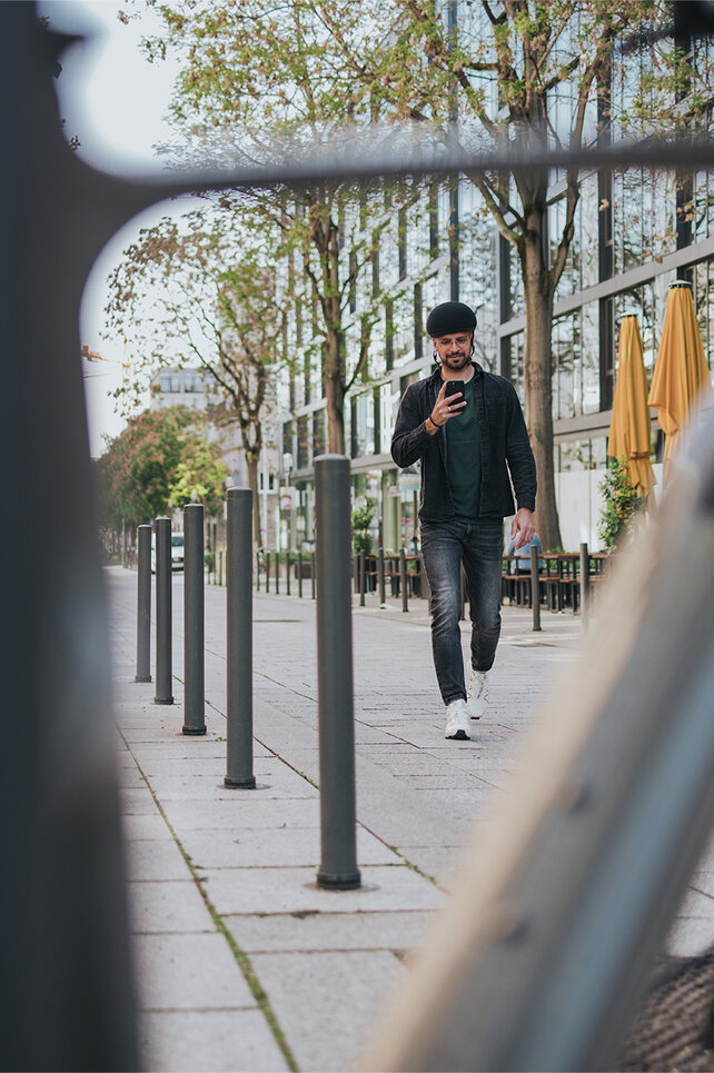 Mężczyzna podchodzi do swojego roweru elektrycznego w mieście i spogląda na swój smartfon.