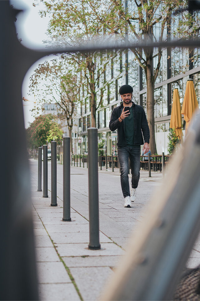 De man loopt in de stad naar zijn e-bike en kijkt op zijn smartphone.