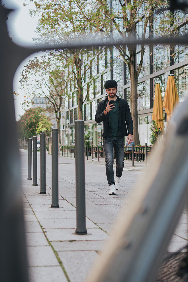 Mann läuft in der Stadt auf sein eBike zu und schaut auf sein Smartphone.