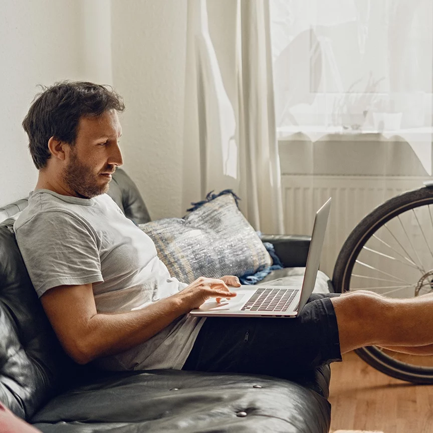 A man sits relaxed on a couch, looking at his laptop.