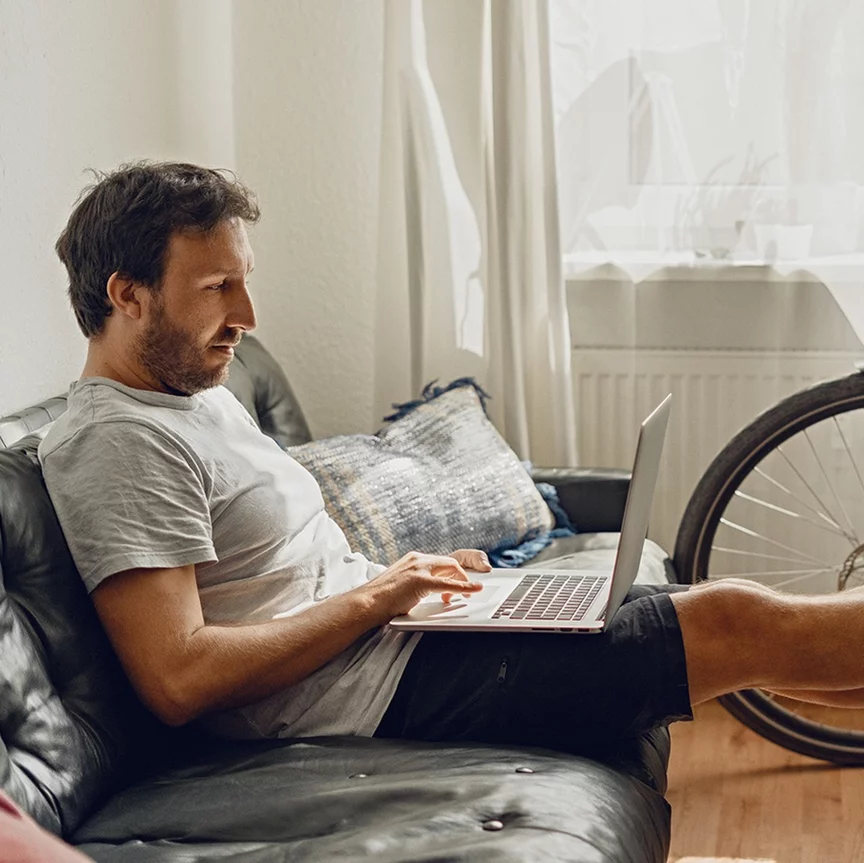 En mann sitter avslappet på en sofa og ser på sin bærbare datamaskin.