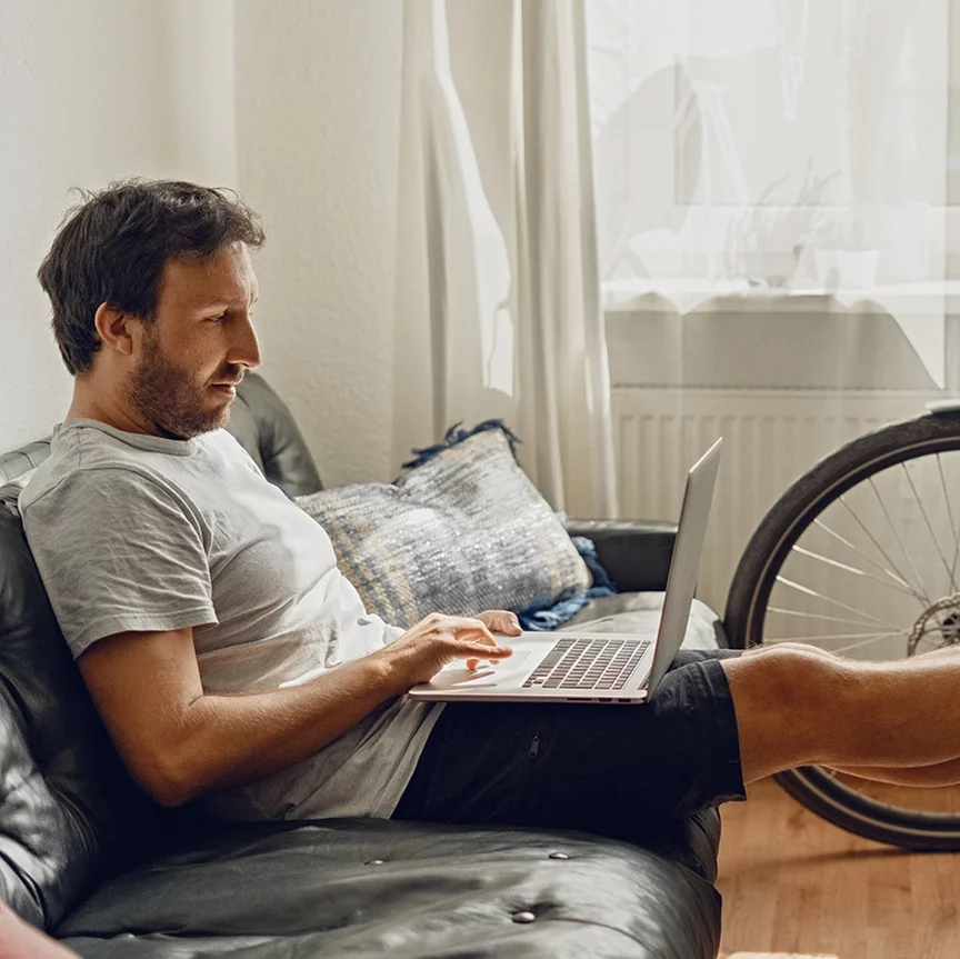 Un homme est assis détendu sur un canapé, en train de regarder son ordinateur portable.
