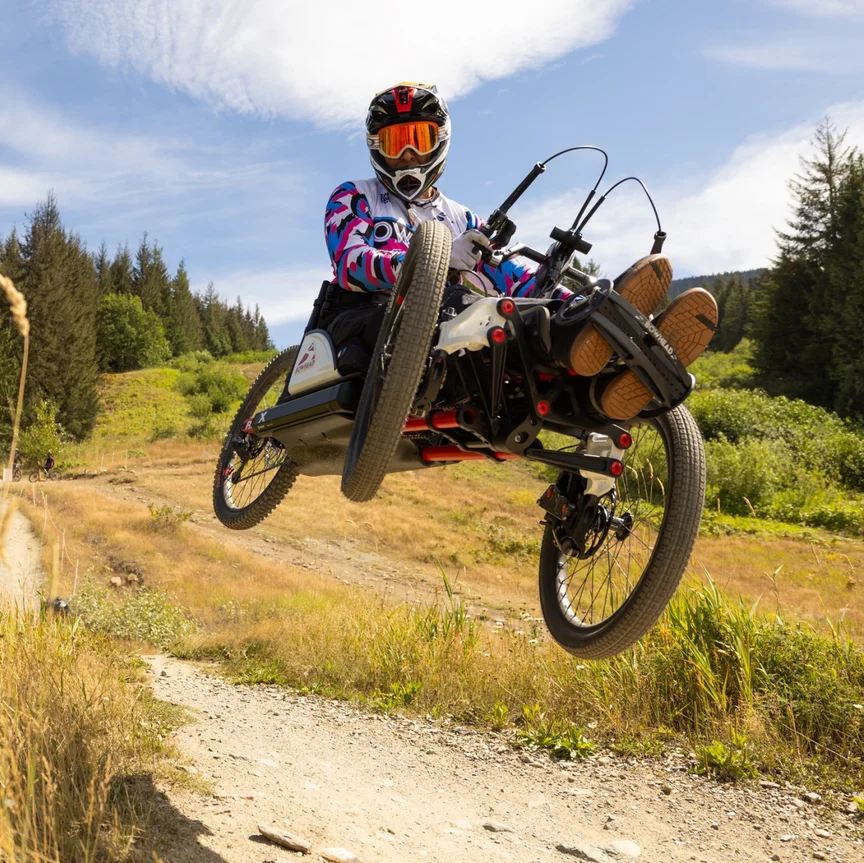Tarek Rasouli rides his handbike along a sunny forest trail, wearing a helmet and protective gear. 