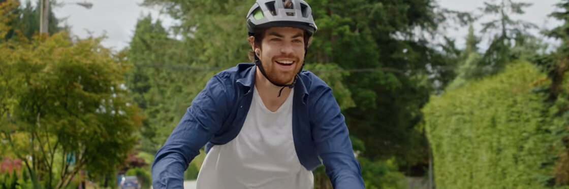 An eBike rider laughs while riding along a road, with trees and hedges visible in the background.