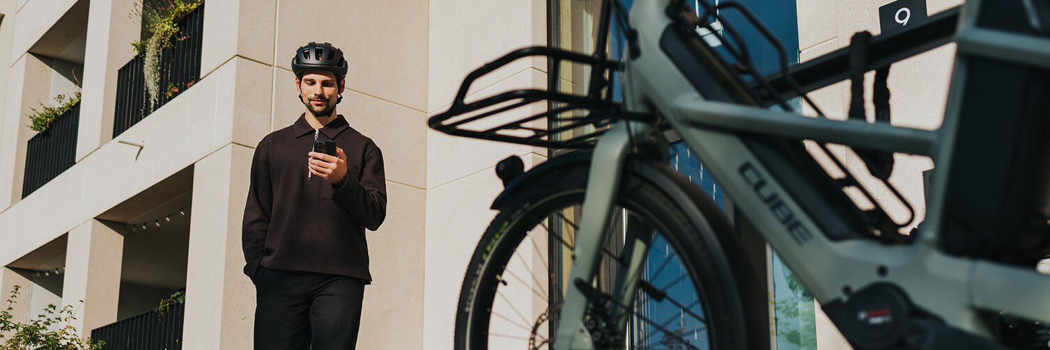 A man in black strides towards an eBike, smiling as he checks his smartphone.