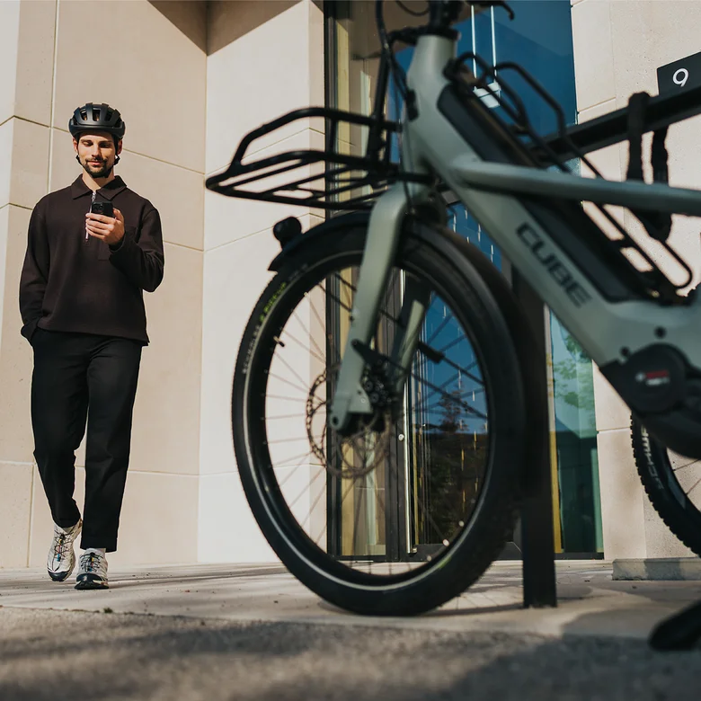 A man in black strides towards an eBike, smiling as he checks his smartphone.
