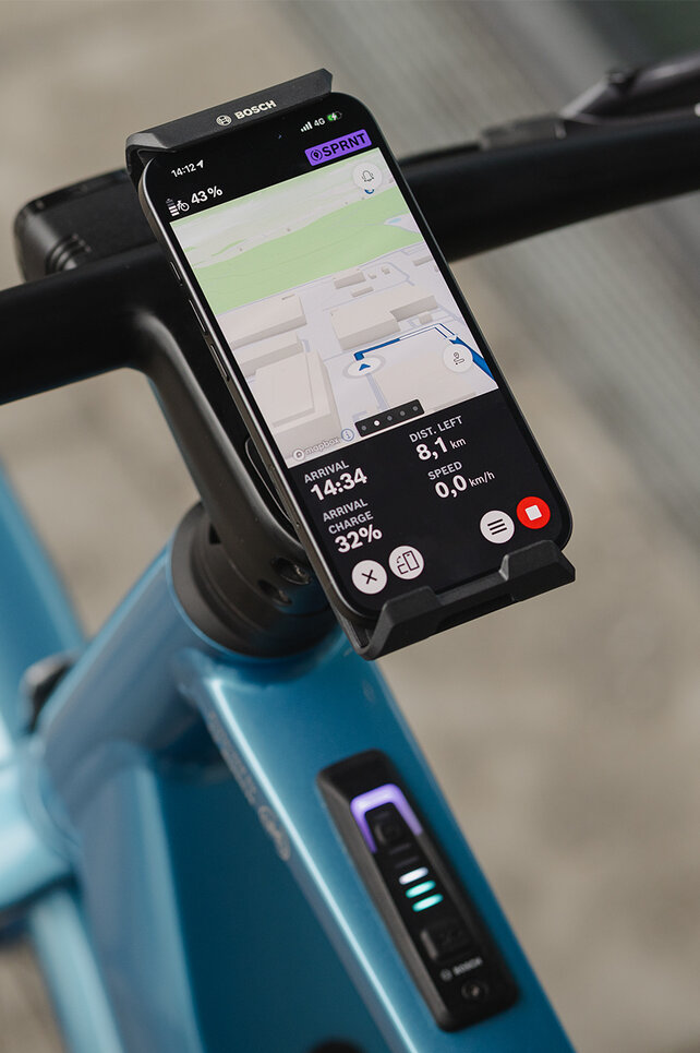Close-up van een SmartphoneGrip die verticaal aan het stuur is bevestigd. De smartphone staat in navigatiemodus en toont een routeweergave.