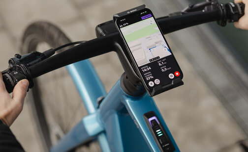 Gros plan sur un SmartphoneGrip vertical fixé au guidon. Le smartphone est en mode navigation et affiche un guidage d’itinéraire.