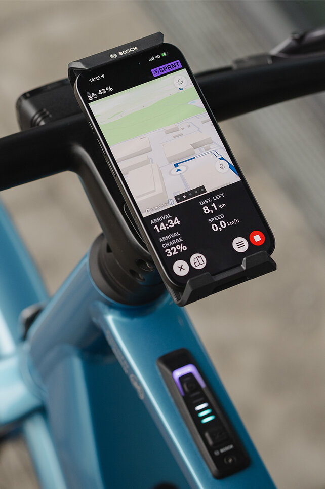 Gros plan sur un SmartphoneGrip vertical fixé au guidon. Le smartphone est en mode navigation et affiche un guidage d’itinéraire.