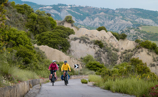 A woman and a man ride their eBikes up a mountain.