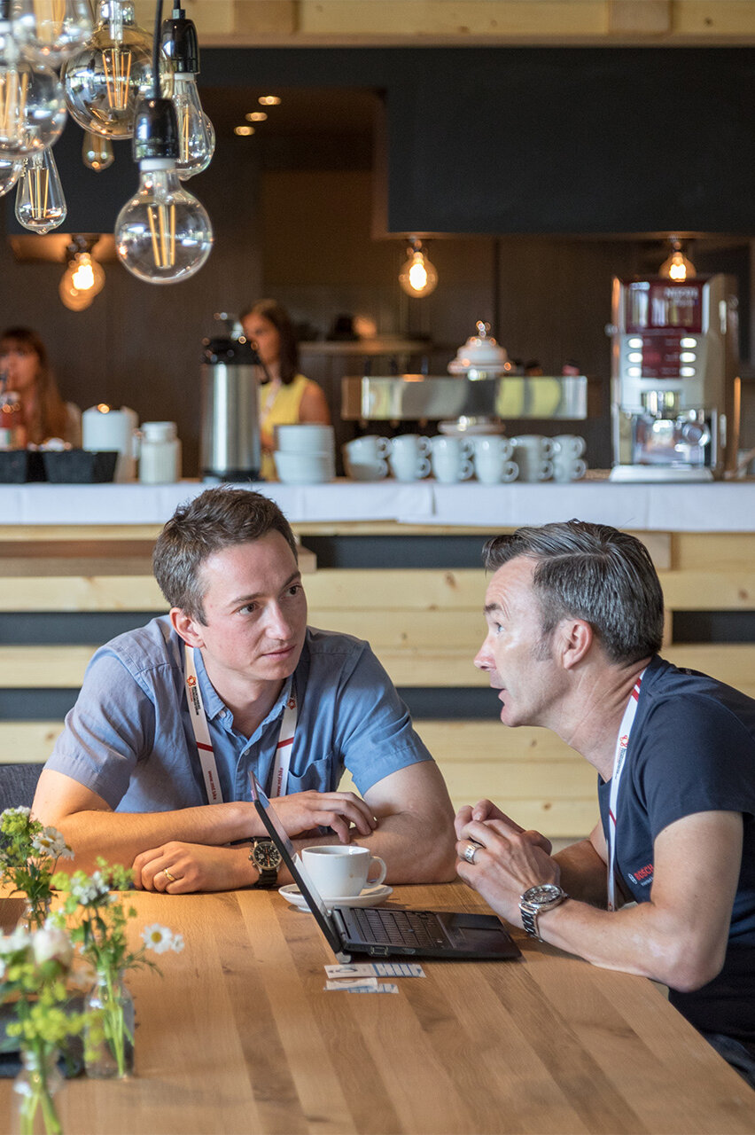Two Men sit at a wooden table in a café and have an intense conversation.