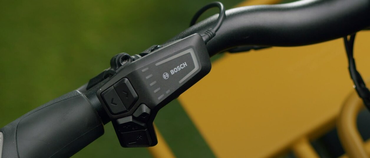 Das Video zeigt wie man das eBike per LED Remote und Smartphone einrichtet. Am Anfang wird der oben sitzende An-Knopf gedrückt, die LEDs blinekn dadurch alle einmal auf. Dann wechselt die Szene. Eine Person hält ein Smartphone, das eine Anleitung anzeigt: "3 Sek. lang drücken, bis die LED blinkt!". Die Person führt diese Anweisung aus und drückt den Knopf 3 Sekunden lang. Anshchließend erscheint auf dem Smartphone Screen die Nachricht "eBike wird eingerichtet"