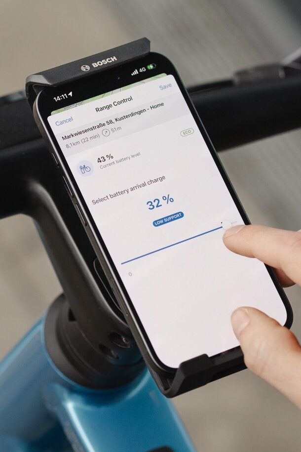 Primer plano de un smartphone que muestra la función Range Control en la aplicación eBike Flow. Un usuario ajusta el nivel de batería deseado al 32 por ciento al llegar a su destino, para optimizar la autonomía en la ruta planificada.