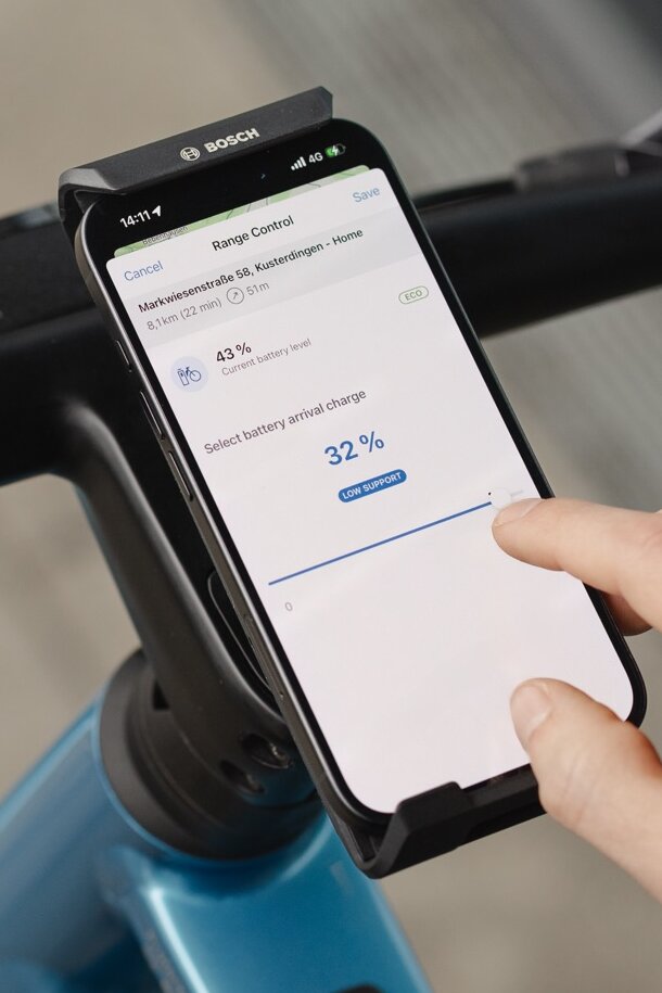 Gros plan d’un smartphone affichant la fonction Range Control dans l’application eBike Flow. Un utilisateur ajuste le niveau de batterie souhaité à 32 % à son arrivée à destination afin d’optimiser l’autonomie pour l’itinéraire prévu.