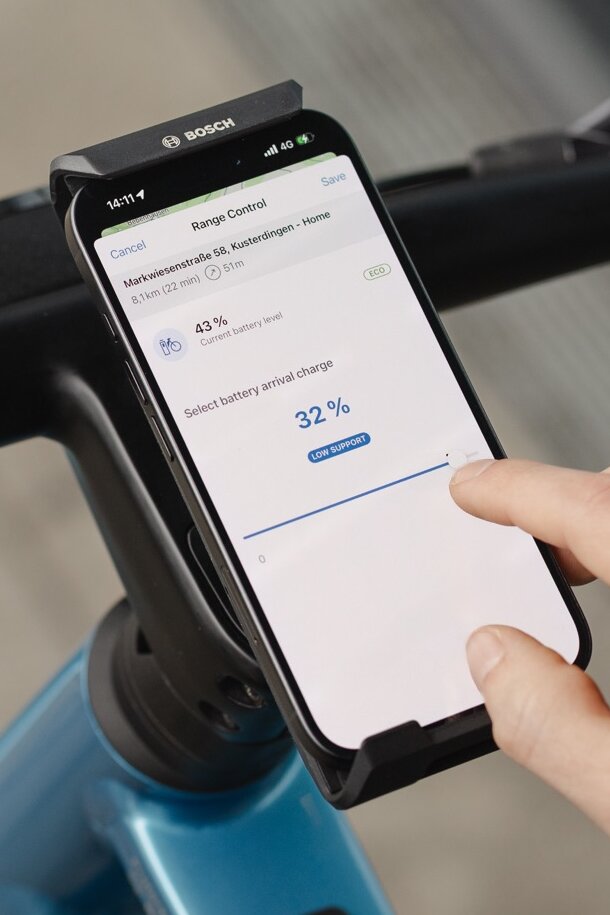 Nærbillede af en smartphone, der viser funktionen Range Control i eBike Flow-app. En bruger justerer det ønskede batteriniveau til 32 procent ved ankomst til destinationen via en skyder for at optimere rækkevidde på den planlagte rute.
