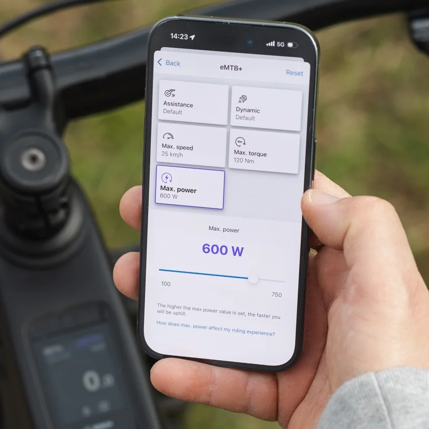 Zbliżenie smartfona pokazujące aplikację eBike Flow do personalizacji trybów jazdy. Ekran wyświetlacza przedstawia opcje ustawień dla trybu eMTB+, gdzie maksymalna moc jest regulowana do 600 watów za pomocą suwaka.