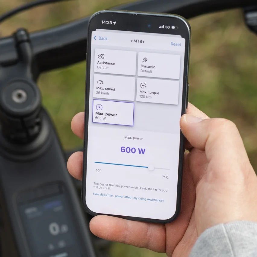 Close-up van een smartphone die de eBike Flow-app toont voor het aanpassen van rijmodi. Het beeldscherm laat de instellingen zien voor de eMTB+-modus, waarbij je het maximale vermogen via een schuifregelaar instelt op 600 watt.