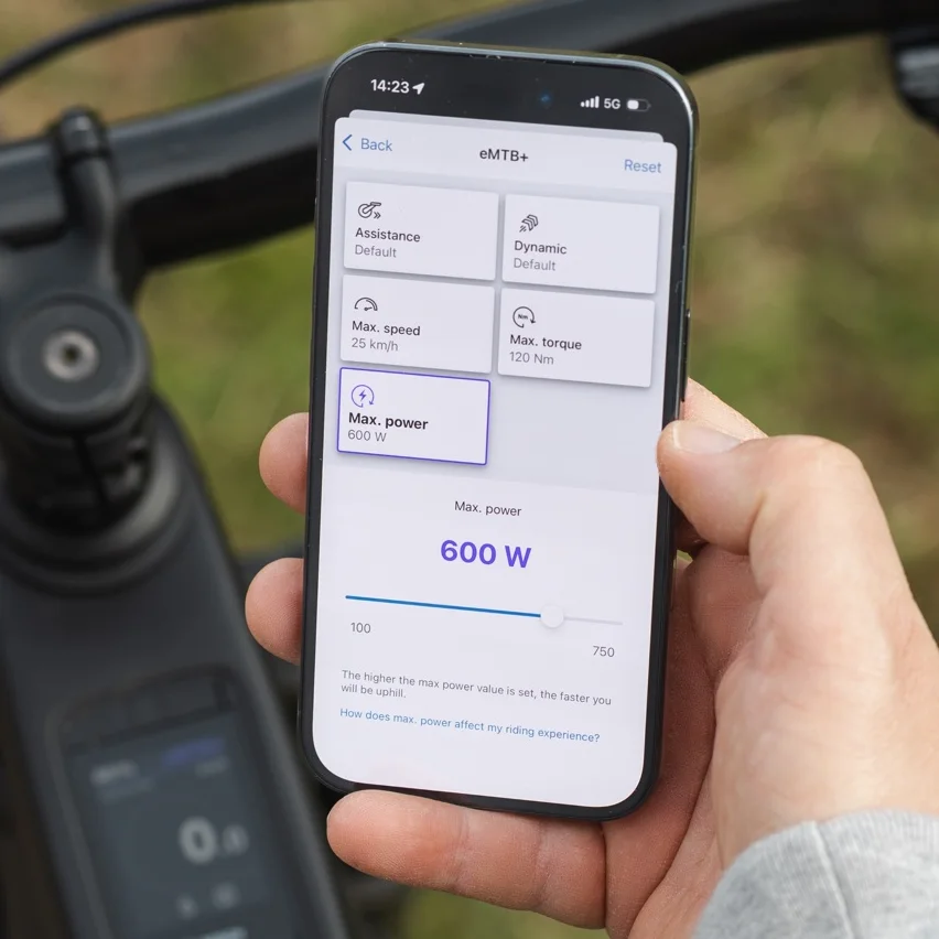 Primo piano di uno smartphone che mostra l'app eBike Flow per personalizzare le modalità di guida. Lo schermo visualizza le opzioni di impostazione per la modalità eMTB+, dove il valore della potenza massima viene regolato a 600 watt tramite un cursore.