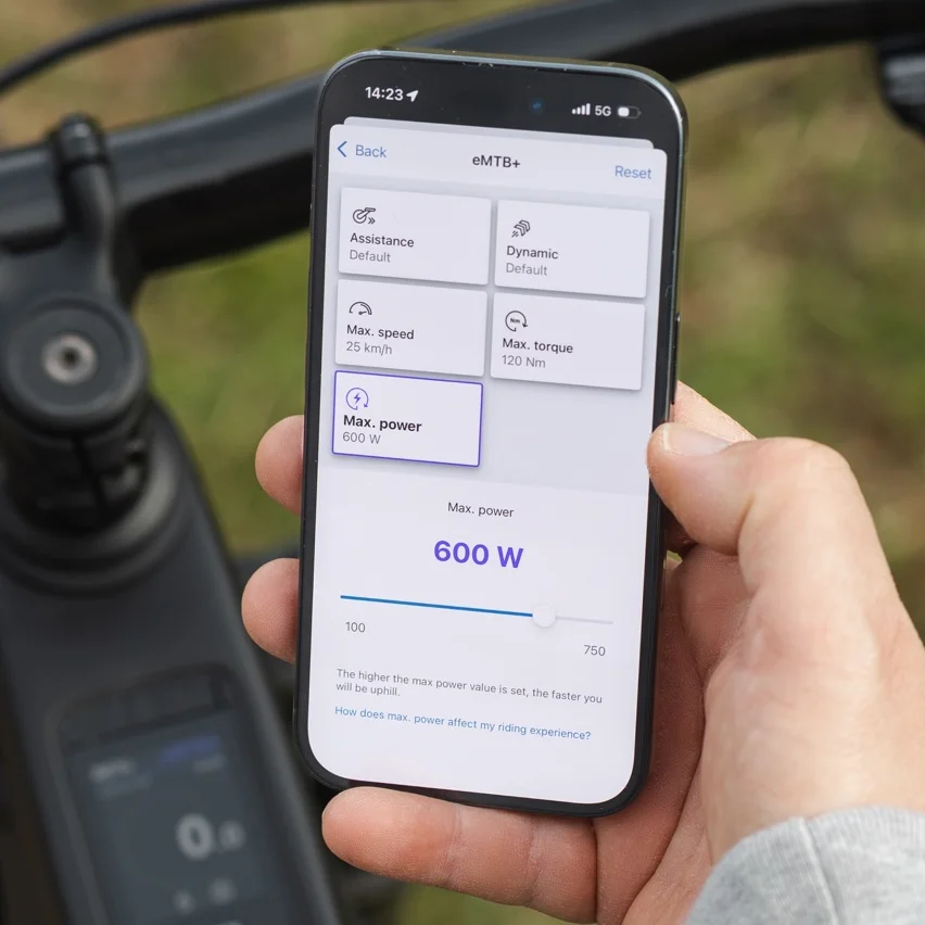 Close-up of a smartphone displaying the eBike Flow app for customizing riding modes. The display screen shows the setting options for the eMTB+ mode, where you can adjust the maximum power to 600 watts using a slider.
