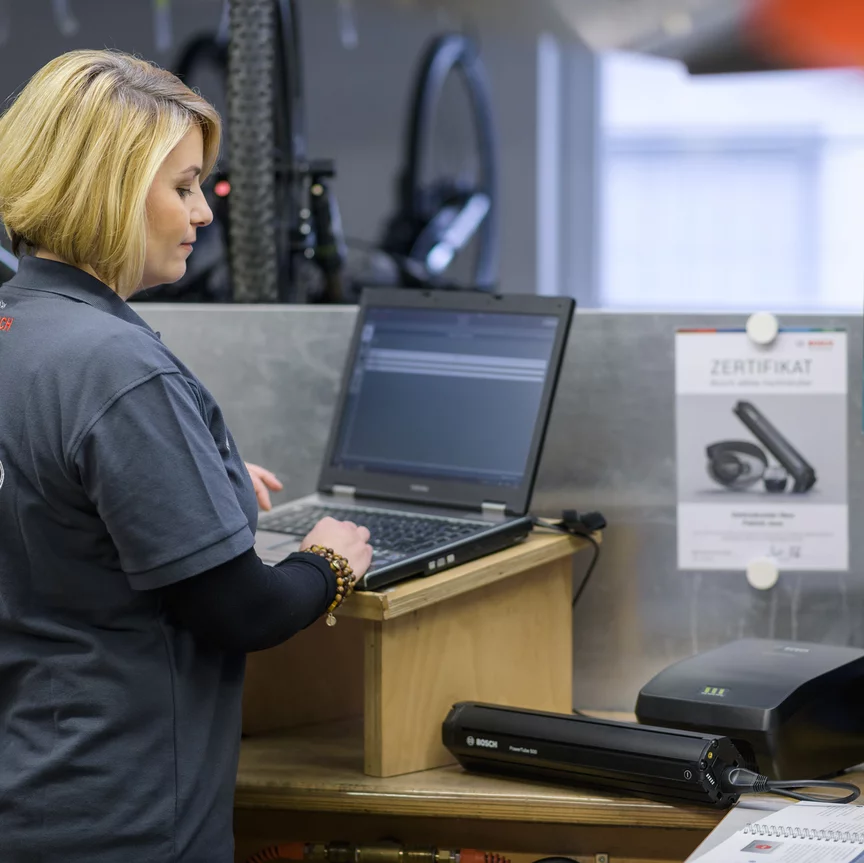 A Bosch eBike dealer looks at an eBike battery in the bike shop and types something into her laptop.