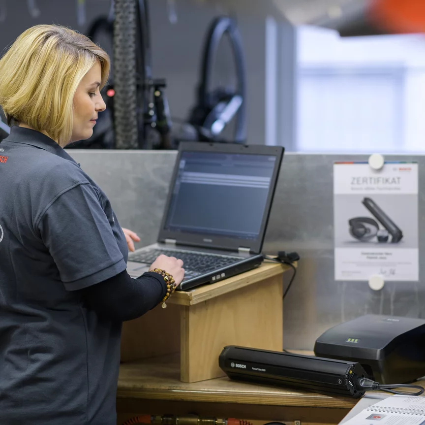 A Bosch eBike dealer looks at an eBike battery in the bike shop and types something into her laptop.