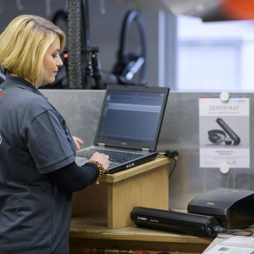 Una rivenditrice di eBike Bosch osserva una batteria per eBike nel negozio di biciclette e digita qualcosa sul suo laptop.