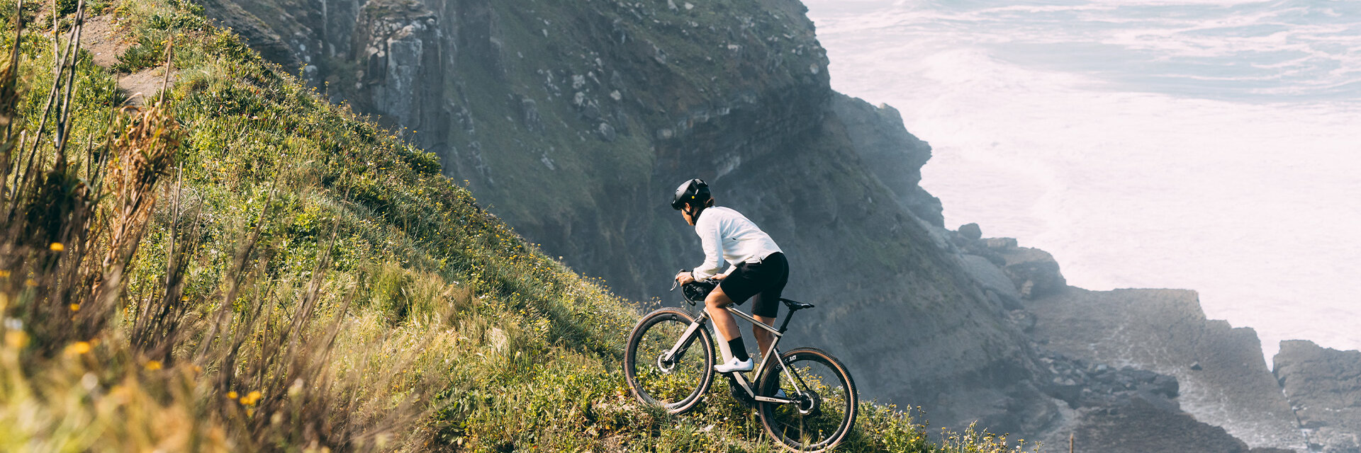 The eBike rider drives up a steep, grass-covered mountain, in the background you can see more mountains.