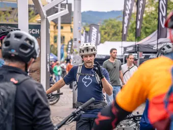 An eBike event: a man in cycling gear talks to two others who are standing opposite him, their backs to the camera.