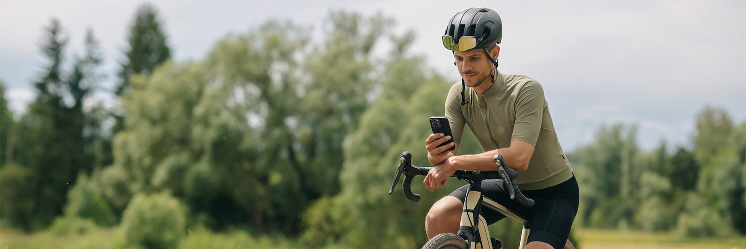 Muž si dává přestávku na svém eBiku, kouká na svůj chytrý telefon. V pozadí jsou vidět louky a lesy.