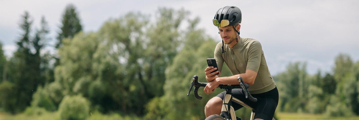 Un hombre se toma un descanso en su eBike y mira su teléfono móvil. Al fondo se pueden ver prados y bosques.