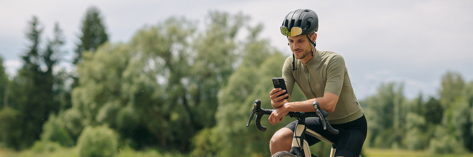 Mann macht eine Pause auf seinem eBike, schaut in sein Smartphone. Im Hintergrund sind Wiesen und Wald zu sehen.