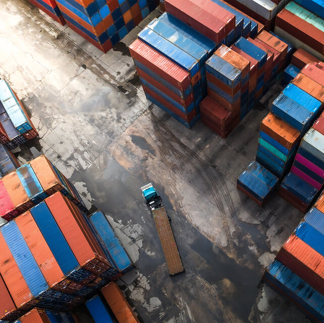 Bird's eye view of a square with several stacked containers and a truck driving with one of these containers.