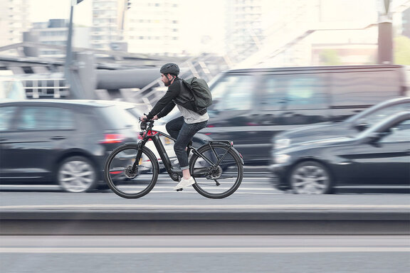eBike Fahrer fährt auf einer vielbefahrenen Straße, die Autos im Hintergrund sind verschwommen.