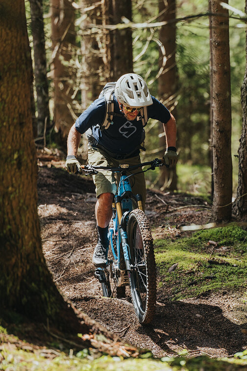 A forest with an eBiker riding uphill on a dirt forest trail.