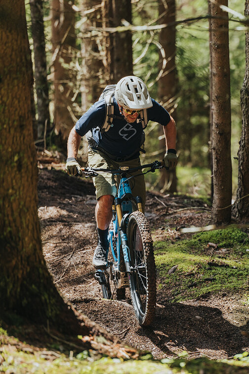 A forest with an eBiker riding uphill on a dirt forest trail.