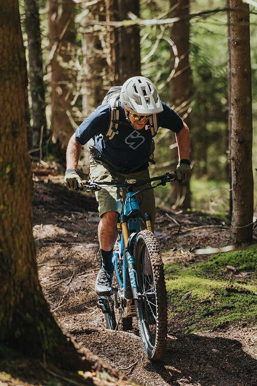 Ein Wald mit einem eBiker, der auf einem erdigen Waldweg bergauf fährt.