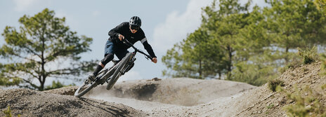 A man is riding quickly down an outdoor trail, with the front wheel of his eBike in the air. Trees are visible in the background.