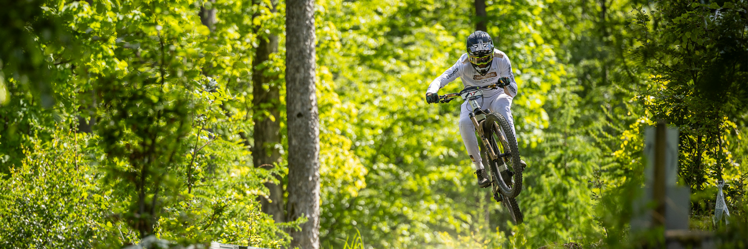 A man jumps with his eMountain bike through the air in the forest while participating in an eMountain bike race.