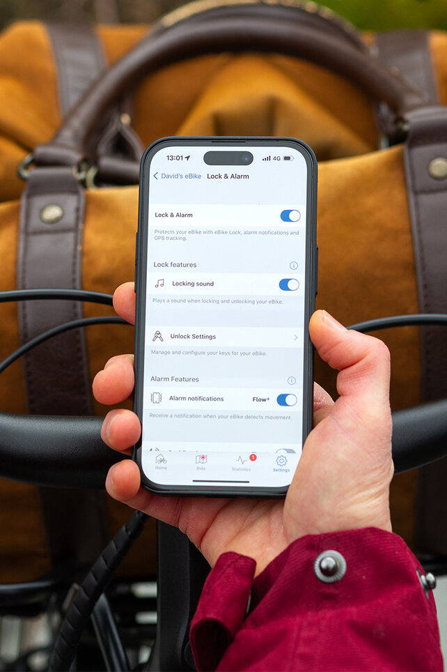 Looking over the shoulder of a person holding a smartphone and adjusting settings for eBike Lock and the alarm in the eBike Flow app.