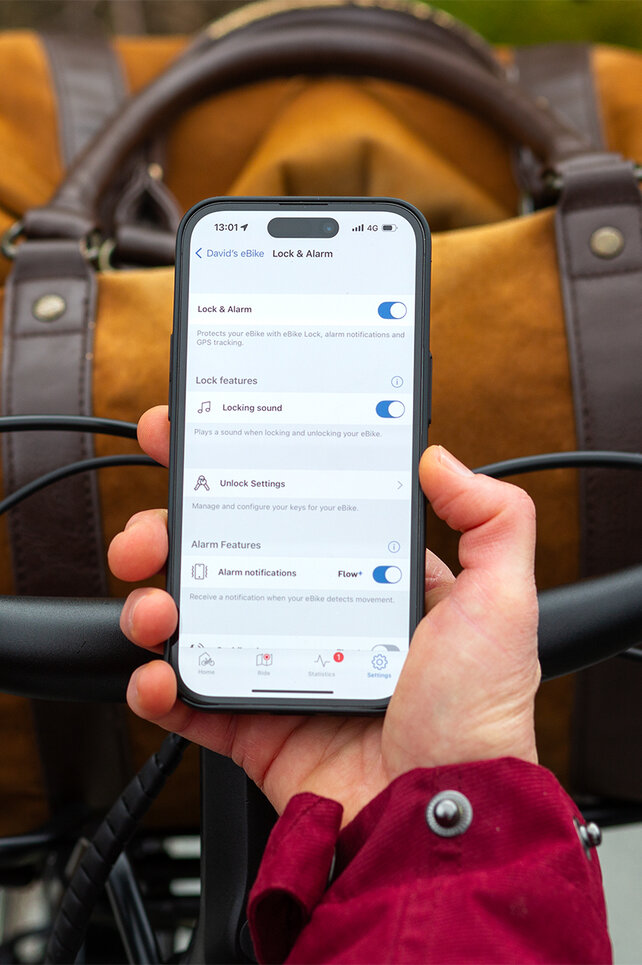 Pohled přes rameno na osobu, která drží chytrý telefon a nastavuje eBike Lock a alarm v aplikaci eBike Flow.