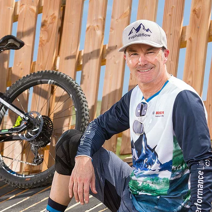 Claus Fleischer, Managing Director of Bosch eBike Systems, smiles for the camera. In the background, a fence and the rear part of an eBike are visible.