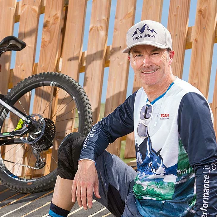 Claus Fleischer, Managing Director of Bosch eBike Systems, smiles for the camera. In the background, a fence and the rear part of an eBike are visible.