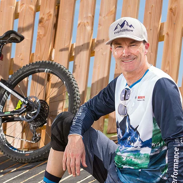 Claus Fleischer, Geschäftsleiter von Bosch eBike Systems, lächelt in die Kamera. Im Hintergrund sind ein Zaun und der hintere Teil eines eBikes zu sehen.