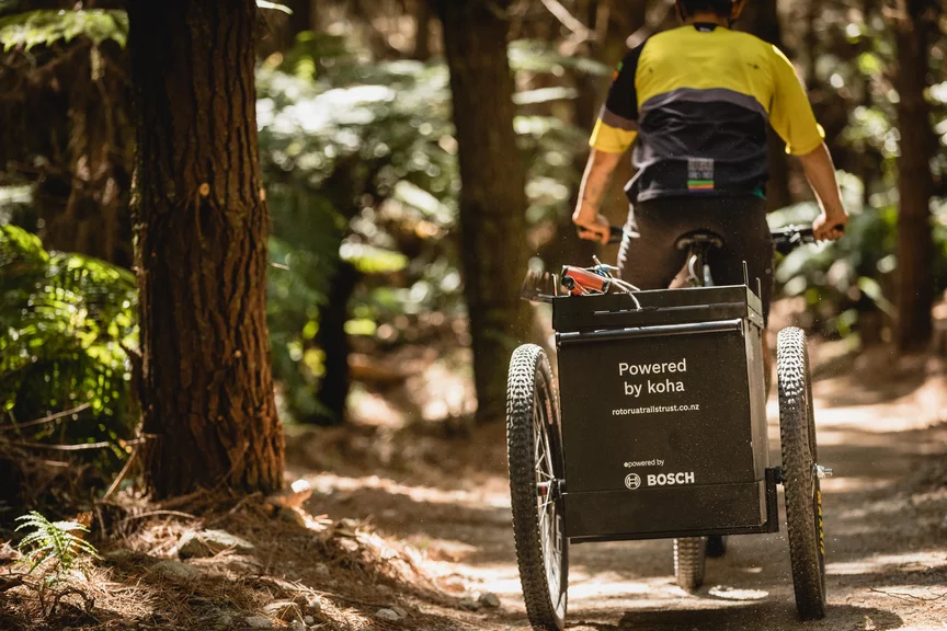 A Cargo eBike rider travels through a forest; on the cargo basket, you can see 'Powered by koha' and the Bosch logo.