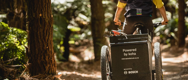 A Cargo eBike rider travels through a forest; on the cargo basket, you can see 'Powered by koha' and the Bosch logo.