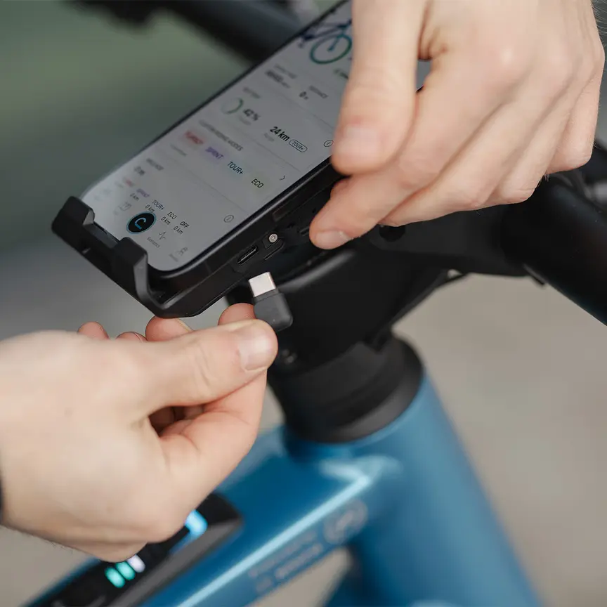 Close-up of an eBike handlebar with a smartphone secured in the SmartphoneGrip Vertical, as a USB-C® cable is being plugged in.